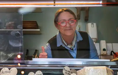 Maja bakom ostdisken med ett leende och tummen upp, omgiven av…